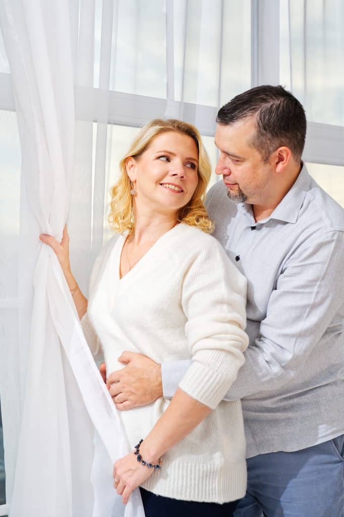 Middle-aged couple embracing in front of window. Middle aged blond woman and man portrait